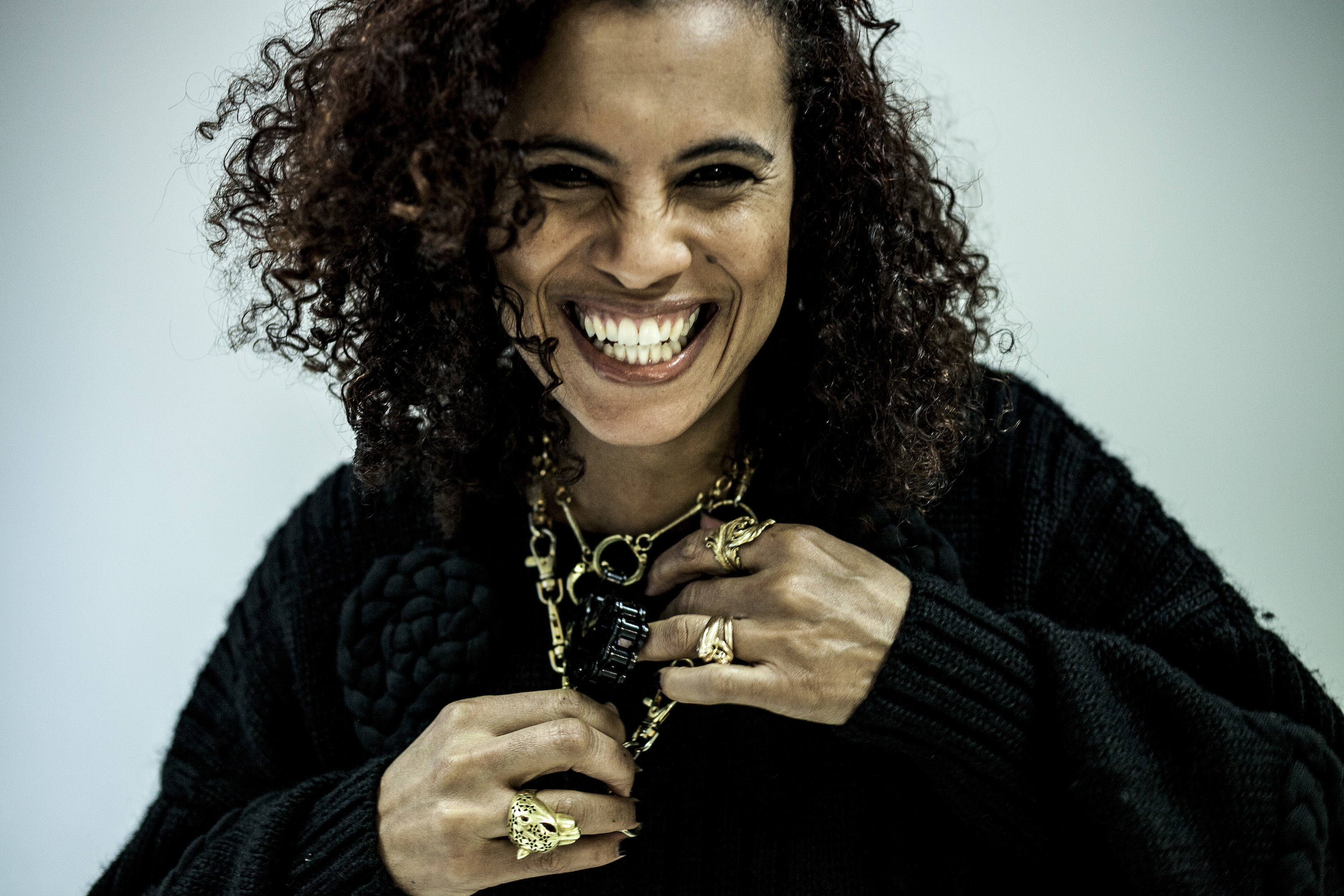 Neneh Cherry lacht in die Kamera. Sie trägt einen schwarzen Pullover und Goldschmuck.